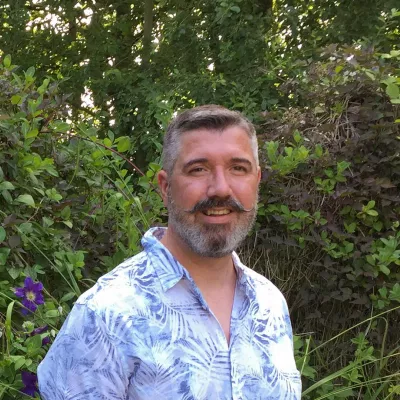 person in blue and white shirt standing in front of green foliage