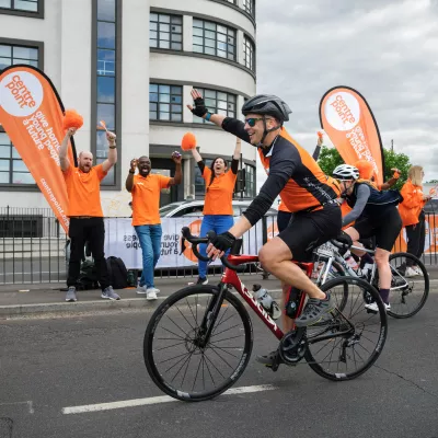 A photograph of a cyclist in a Centrepoint jersey waving at a group of Centrepoint roadside cheerleaders