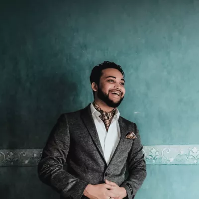 Young person smiling wearing a grey suit against a teal coloured wall