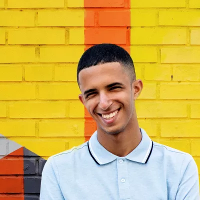 Young person smiling against a yellow brick wall