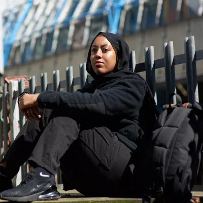 Young person sitting near a fence with a rucksack