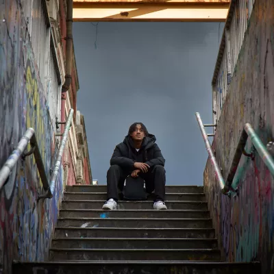 Young person sitting outside on some steps with a rucksack