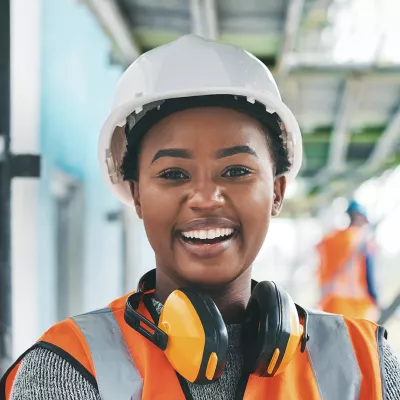 Young person wearing a hard hat on a construction site smiling and looking directly at the camera