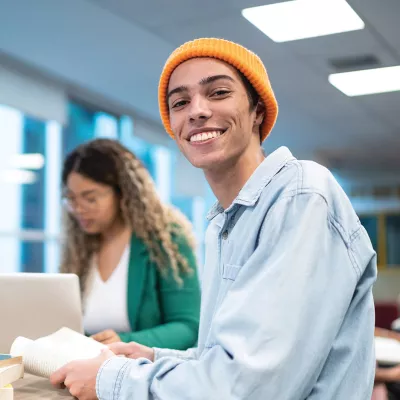 Young person wearing orange beanie sitting at a desk and smiling