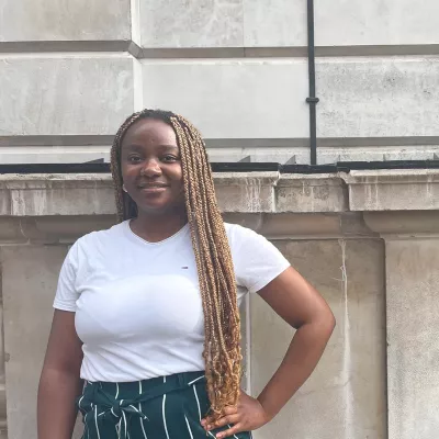 Young woman with one hand on her hip wearing a white t shirt standing outside a building