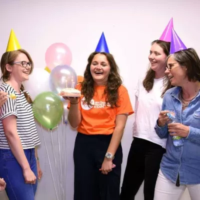 People wearing party hats, someone holding a cake