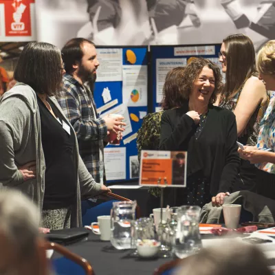 People talking to each other at the National Youth Homelessness Conference - a pin board can be seen in the background with documents on it.