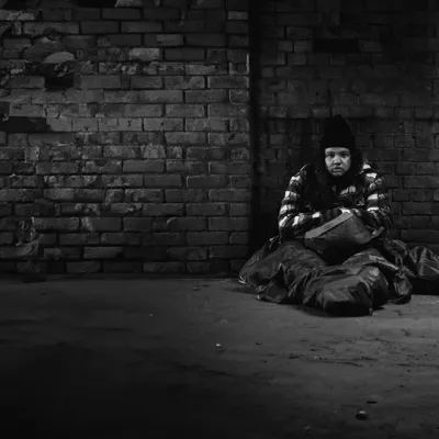 black and white image of Mia who is sat outside on the floor, with a sleeping bag, looking cold and homeless
