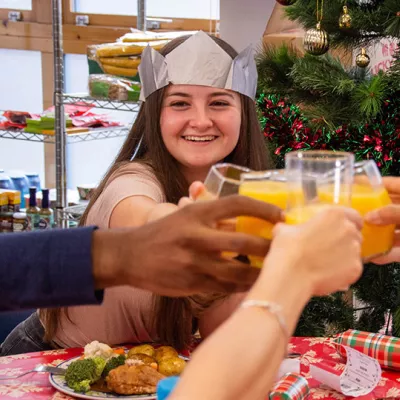 Young people sit around a dinner table wearing Christmas paper crowns, raising their glasses of orange juice for a toast