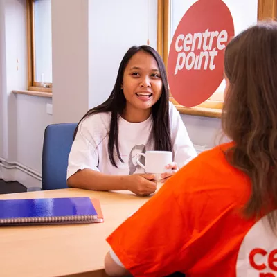 A Centrepoint support officer and a young person sit at a table, drinking a hot drink and chatting