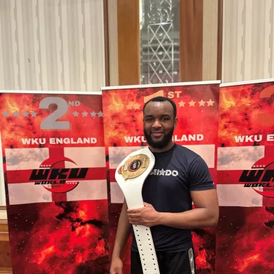 Young person holding a martial arts trophy belt over shouder