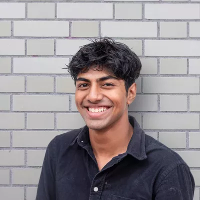 smiling young person standing against a grey brick wall