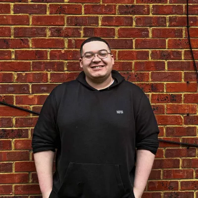 Young person in black hoodie standing against a brick wall.