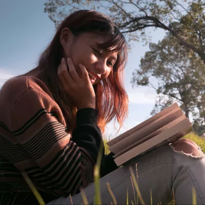 young person sitting in the park with a book