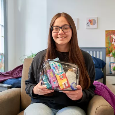 A young person sits in a Centrepoint service, smiling at the camera and holding a collection of toiletries