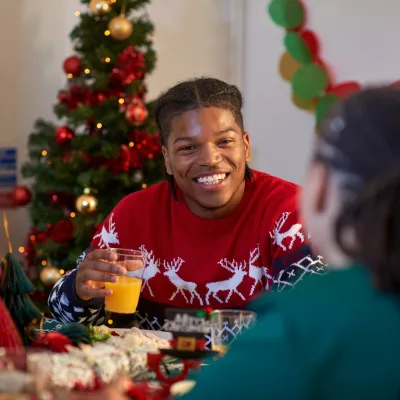 A young person wearing a festive red jumper sits at the dinner table enjoying a Christmas dinner