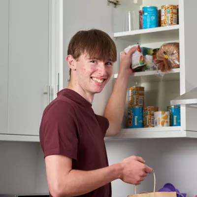 A young person gets food out of a well-stocked kitchen cupboard at home