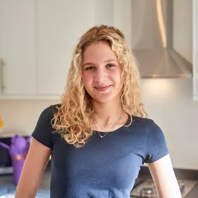 A young person smiles while standing in her kitchen at home