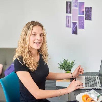 A young person sits and studies at a desk with a laptop and notepad