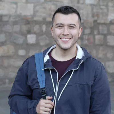 Young person with a backpack in front of a brick wall