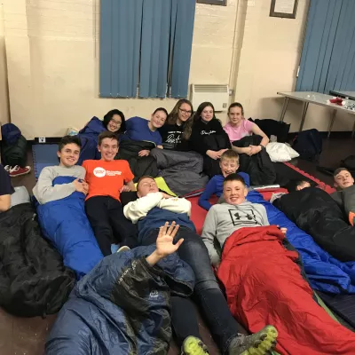 a group of young people lie down in sleeping bags in their classroom