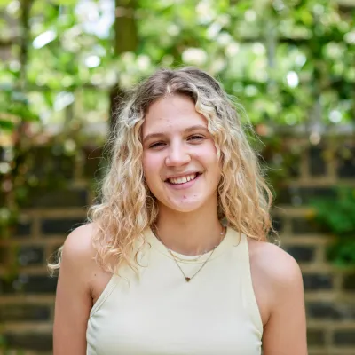 A young person stands outside and smiles at the camera