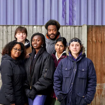 A group of young people affected by homelessness stand together and smile at the camera