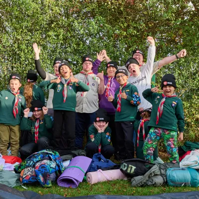 group of cub scouts cheering at the camera in front of sleeping bags and roll mats