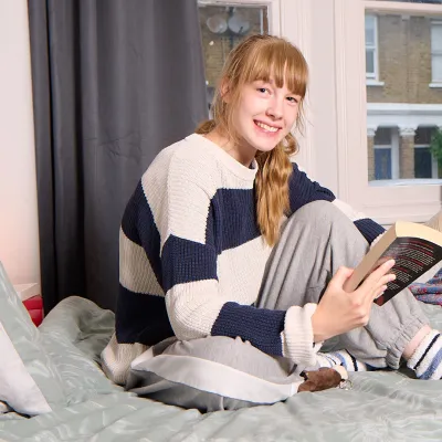 A young person sits on a bed reading in supported accommodation