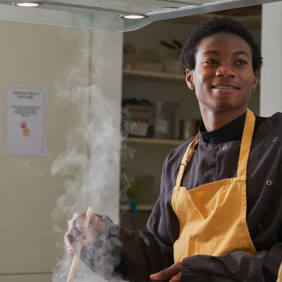 A young person smiles while cooking