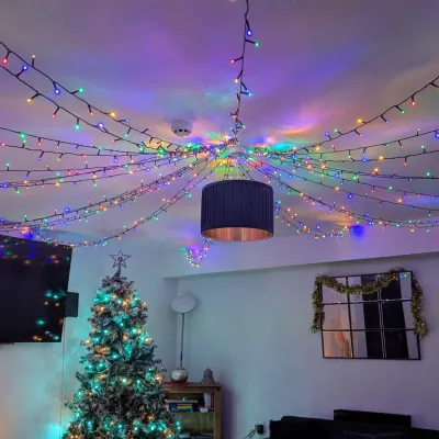 Colourful Christmas lights adorn the ceiling of a living room, with a Christmas tree in the background