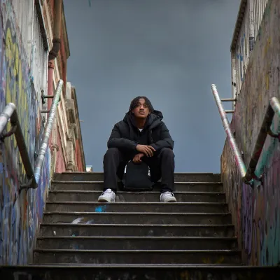 A young person sits at the top of the stairs of an underpass