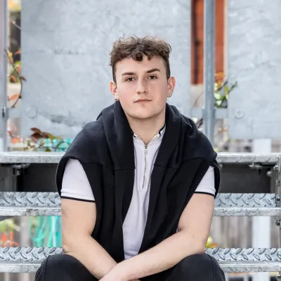 A young person sits on some metal fire escape steps, hidden behind a building where they're less likely to be disturbed