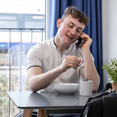 Young person on phone sitting stirring a cup of tea