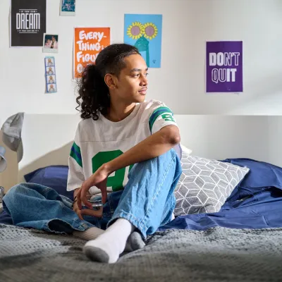 A young person sits on a comfortable bed in their supported housing