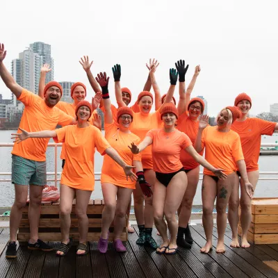 Group of people wearing orange T shirts, raising their hands in the air and cheering.