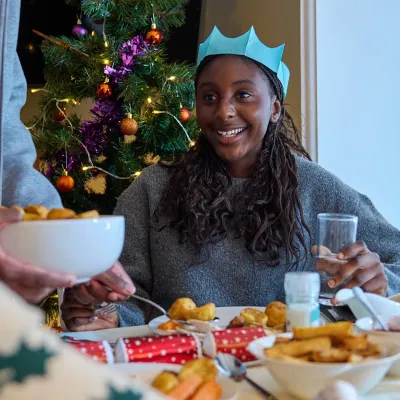 Young people enjoy a christmas dinner at the table, smiling and wearing paper crowns from crackers