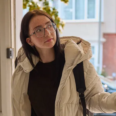 A young person opens the front door and walks into their new flat for the first time