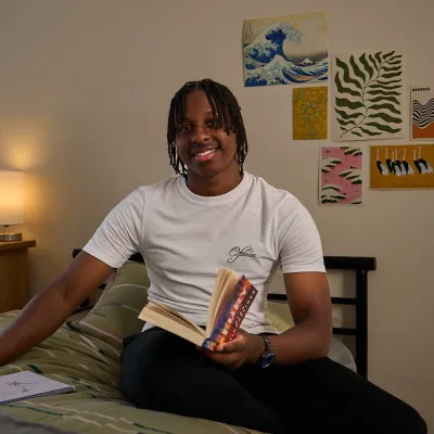 A young person smiles sitting on their bed in their cosy room at a Centrepoint service.