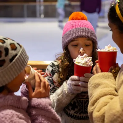 A group of children in warm hats and coats stand together and drink a luxurious takeaway hot chocolate
